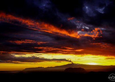 Silhouette of a volcano and its smoke melting in the black and red clouds at sunset