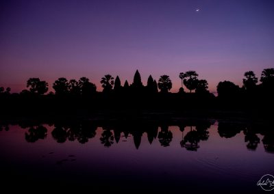 Angkor Wat at sunrise with purple sky and the moon and perfect symetric reflection in the lake