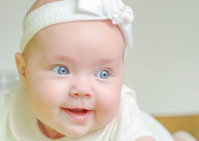 6 month old smiling baby with blue eyes in white dress