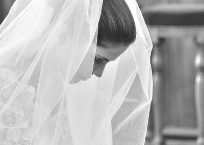 Black and white picture of a bride praying at the church with her veil on