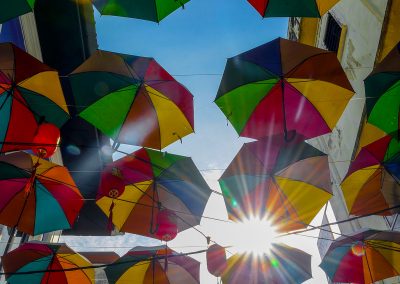 Multiple colorful umbrellas hanging open across a street with a blue sky in background