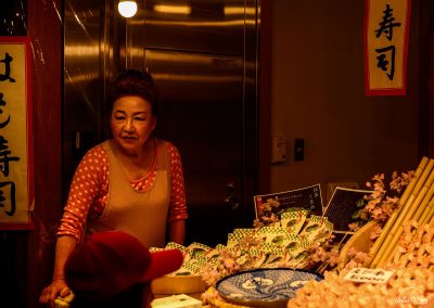 Woman with dotted dress behind her stall of Japanese delicatessen