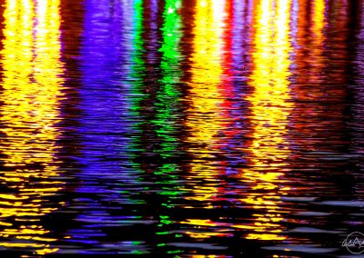 Reflection of the yellow, pink, green, violet lights of shops at night in the dark water