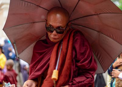 Monk walking in the street covered by an umbrella and with sunglasses