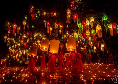 Group of monks lighting lanterns for Yi Peng festival with candles reflecting in the water
