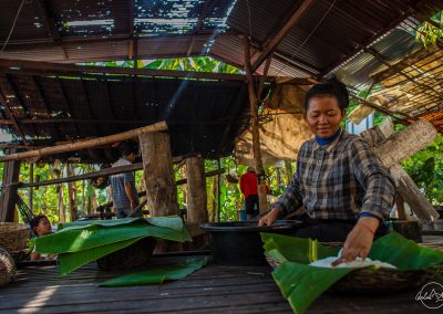 Woman preparing rice noodles in a plate with green leaves and her family in the background