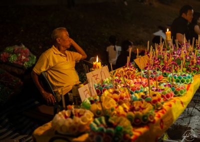 Man sitting at a stall selling Loy Kratong offering at night