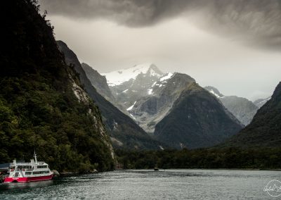White boat on a lake longing huge mountains with snowy mountain in the background and heavy clouds in the sky