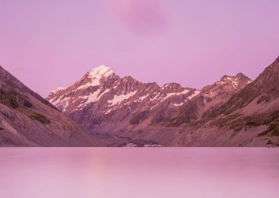 Slow speed capture of a lake and a mountain with fluffy cloud in the sky in a purple and pink hue